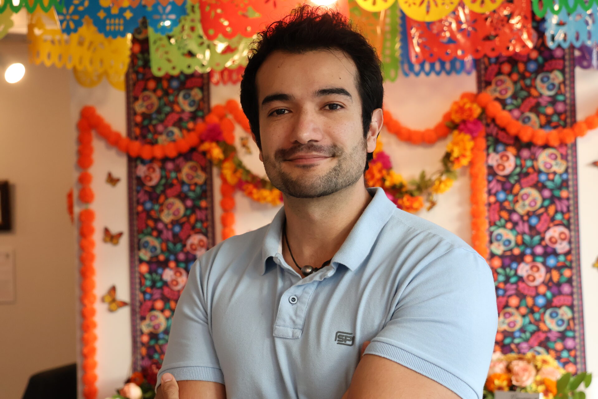 Carlos Iván Ibarra Pacheco, ingeniero de software mexicano que trabaja en Microsoft, posa frente a un colorido fondo de arte tradicional mexicano en el Centro Cultural Mexicano.